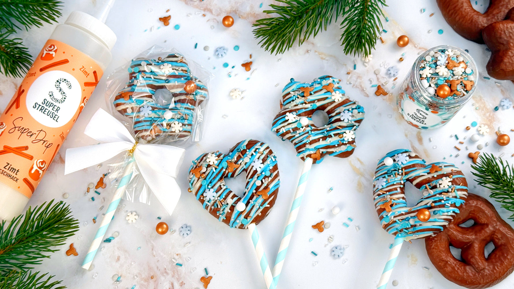 Fertige Lebkuchen verziert mit SuperDrip in verschiedenen Farben und Geschmäckern und getoppt mit weihnachtlichen RentierStreuseln. Die Lebkuchen sind auf einen Stiel gesteckt.