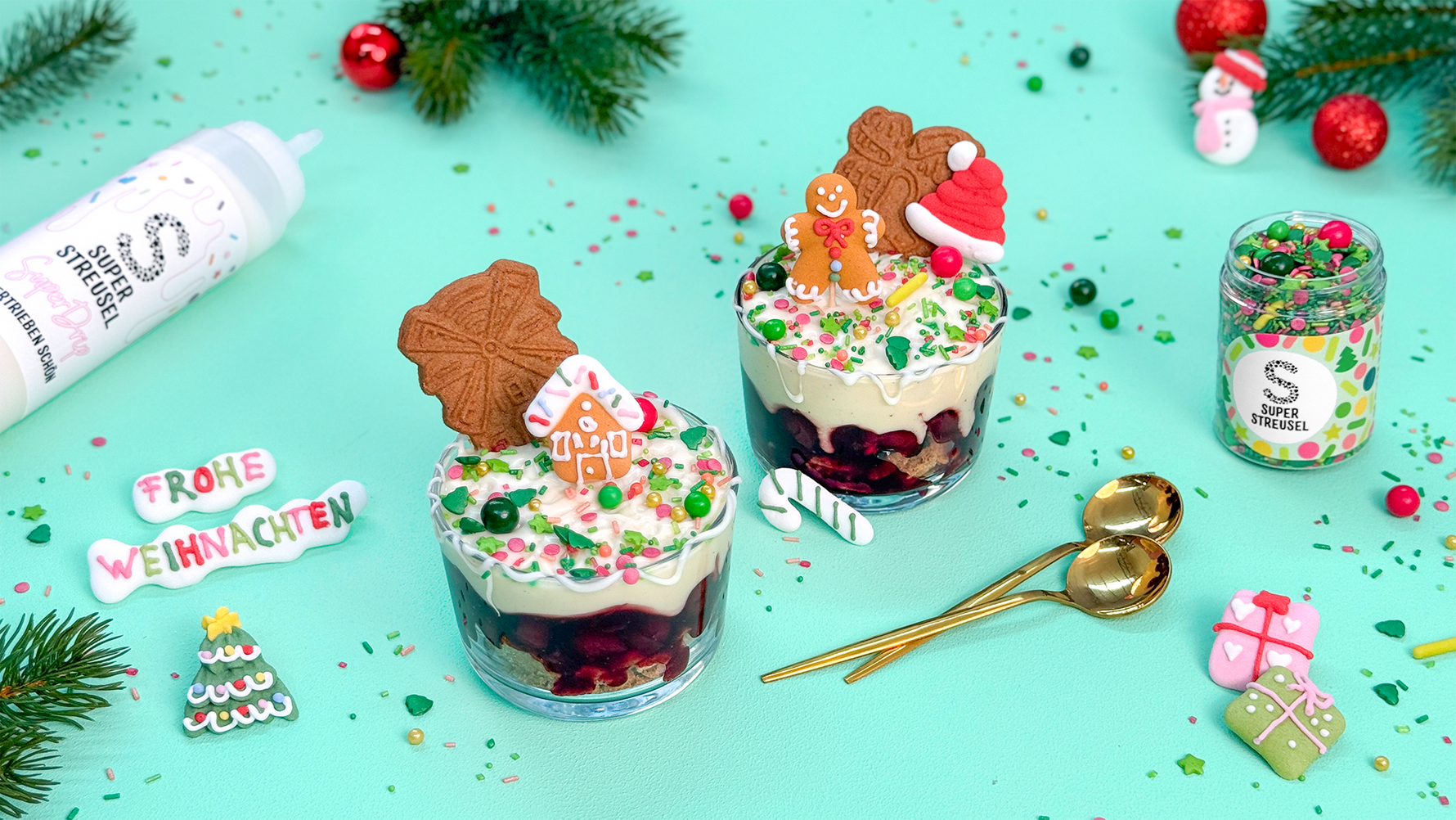 WeihnachtsDessert im Glas jeweils mit einer Schicht Spekulatius-Kekse, Kirschgrütze und cremigem Vanillejoghurt. Darauf verziert weißer SuperDrip, bunte WeihnachtsStreusel und weihnachtliche Zuckerfiguren.
