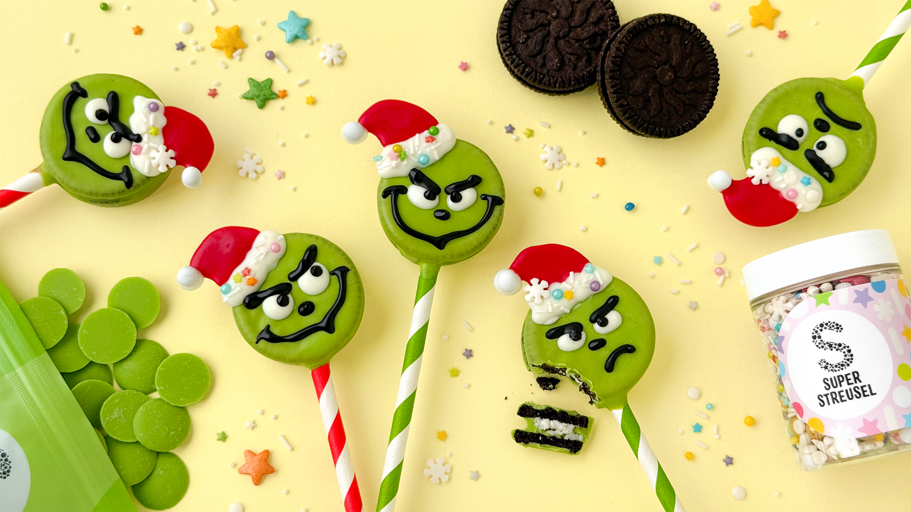 CookiePops im GrinchDesign aus Sandwichcookies auf CakePopStielen mit grünen GrinchGesichtern und weihnachtlicher StreuselMix Deko.